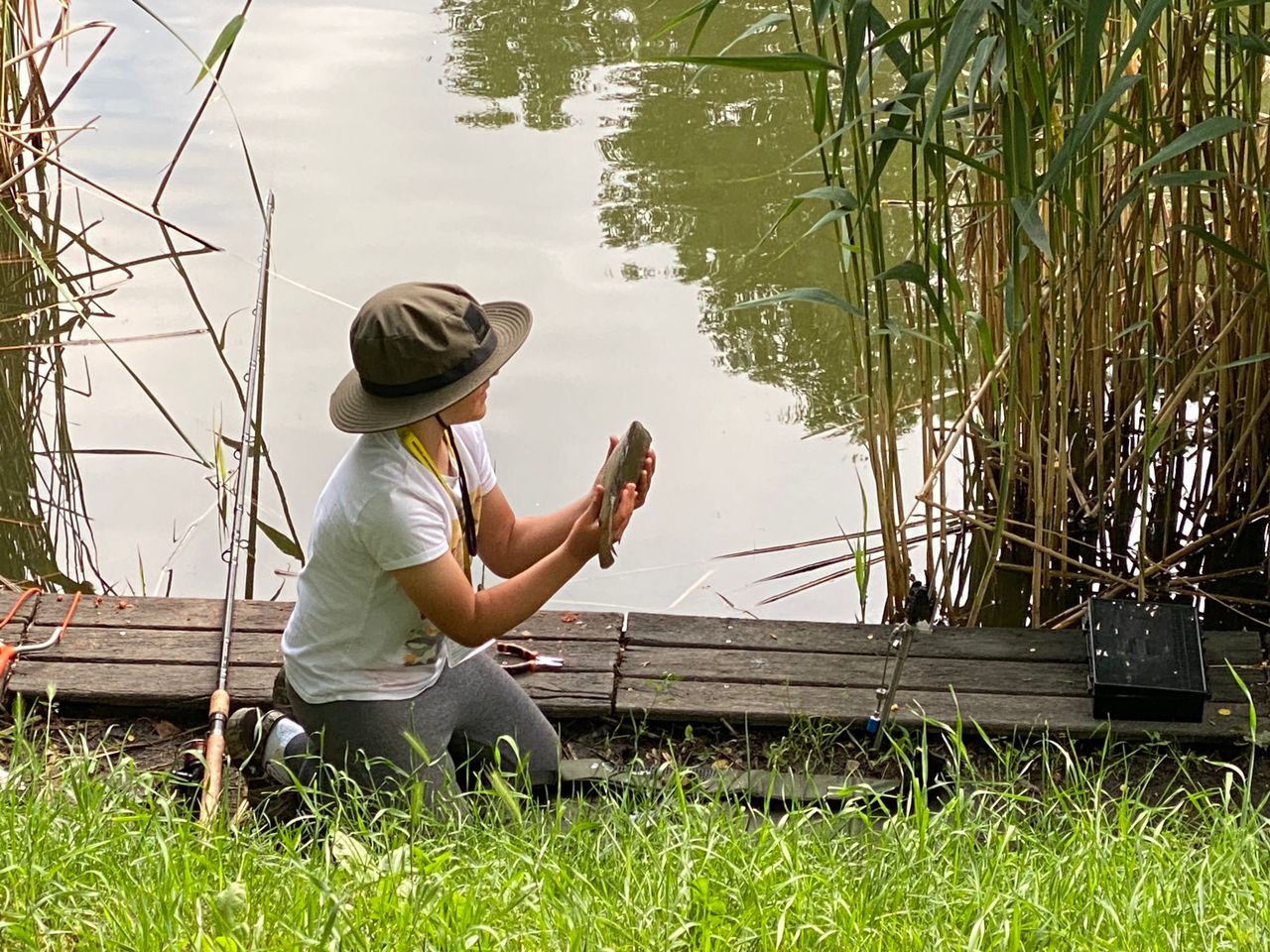 A person holding a fish beside a lake in Poland before releasing it