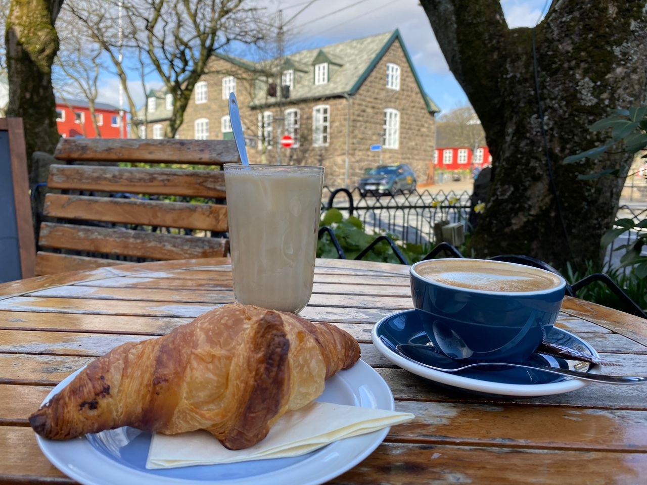 Coffee and croissant in Tórshavn, Faroe Islands, with grass-roof buildings nearby